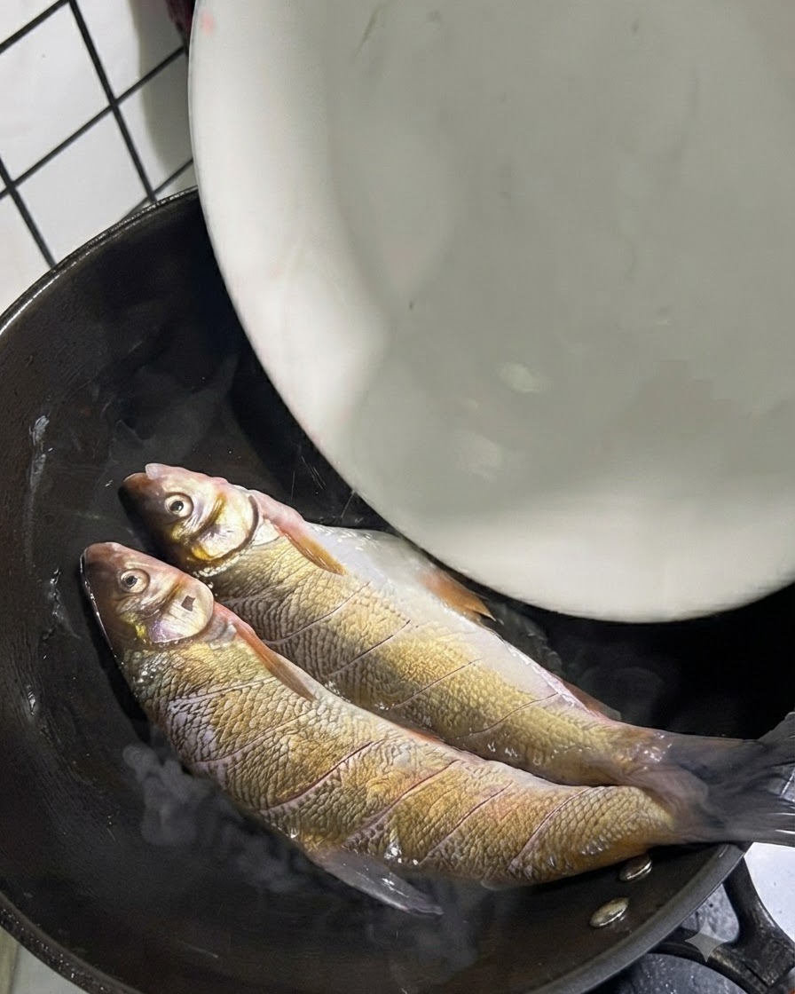 Due pesci coda gialla interi posizionati allinterno di un wok caldo con olio.
