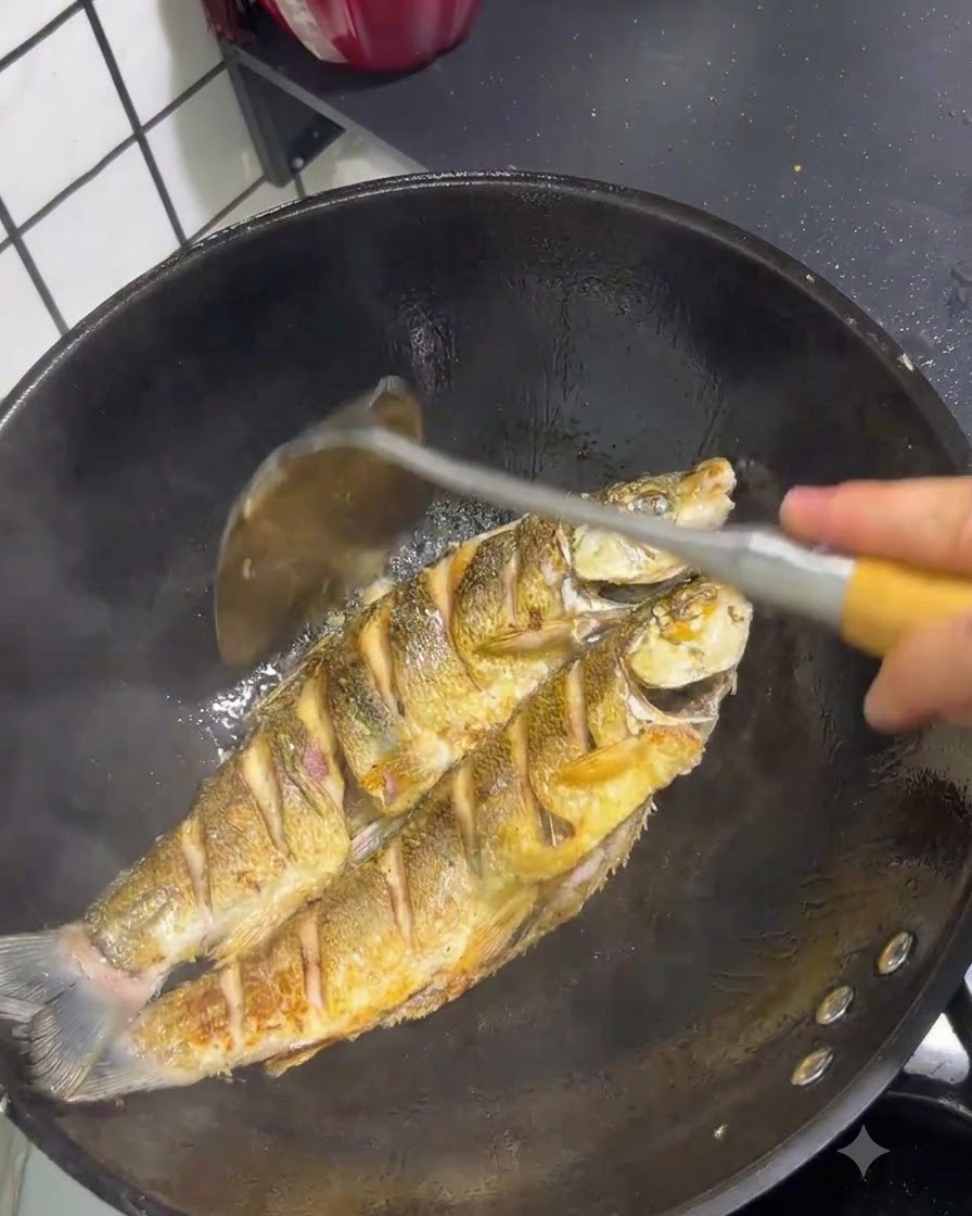 Due pesci coda gialla che friggono in un wok con la pelle dorata gestiti da una spatola.