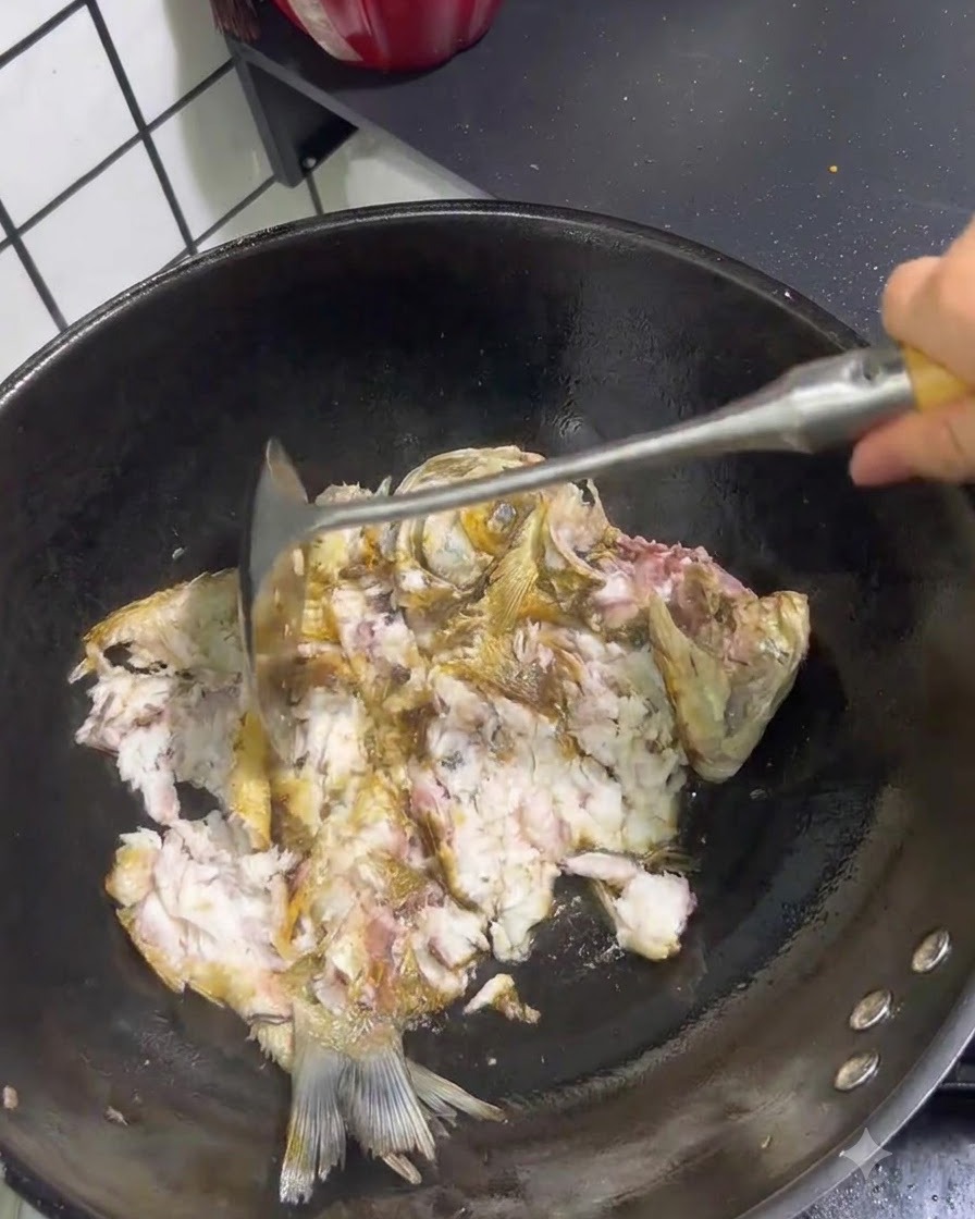 Pesce fritto spezzato e schiacciato con una spatola di metallo allinterno di un wok.