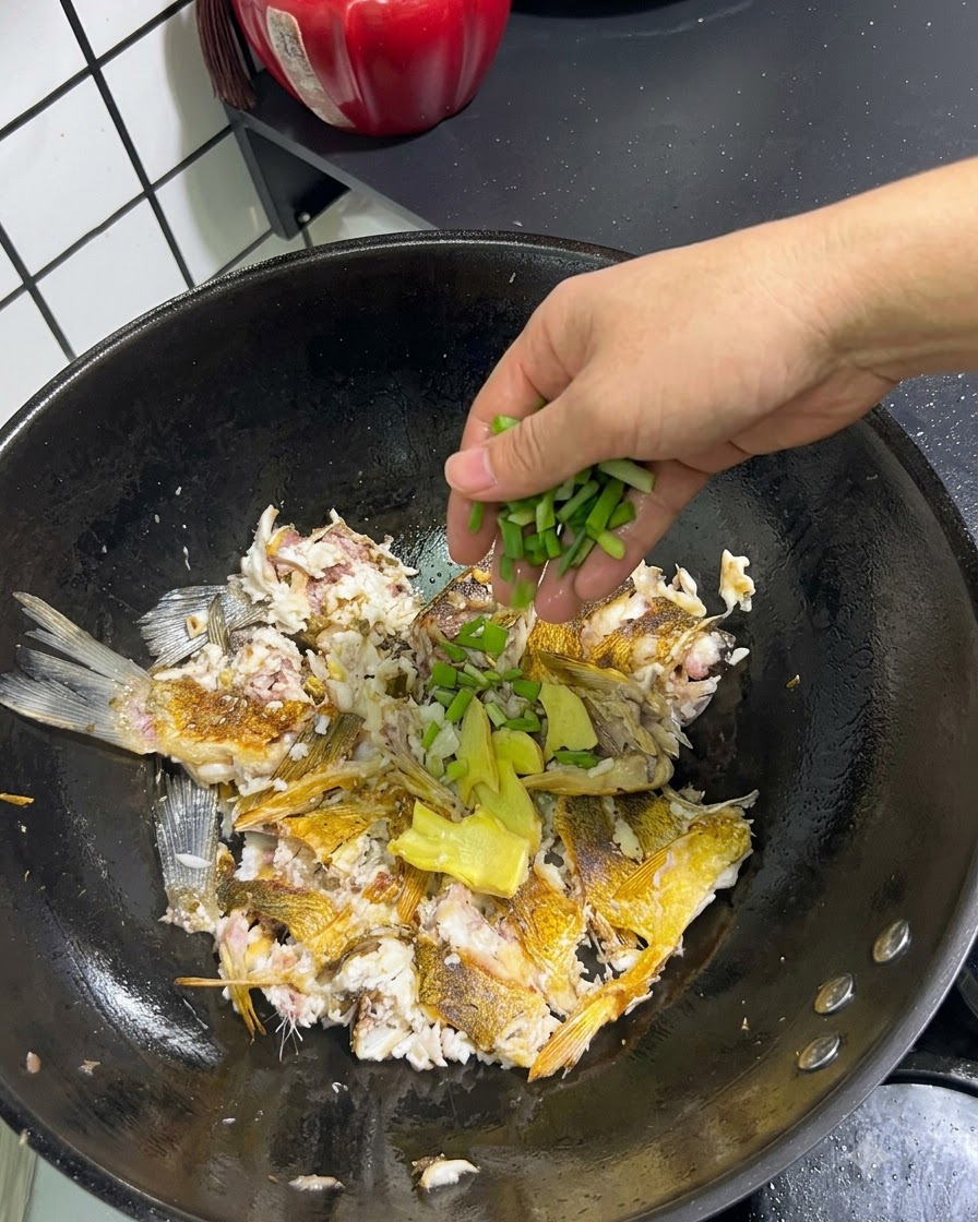 Cipollotti freschi e zenzero affettato aggiunti a mano sopra il pesce schiacciato in un wok.