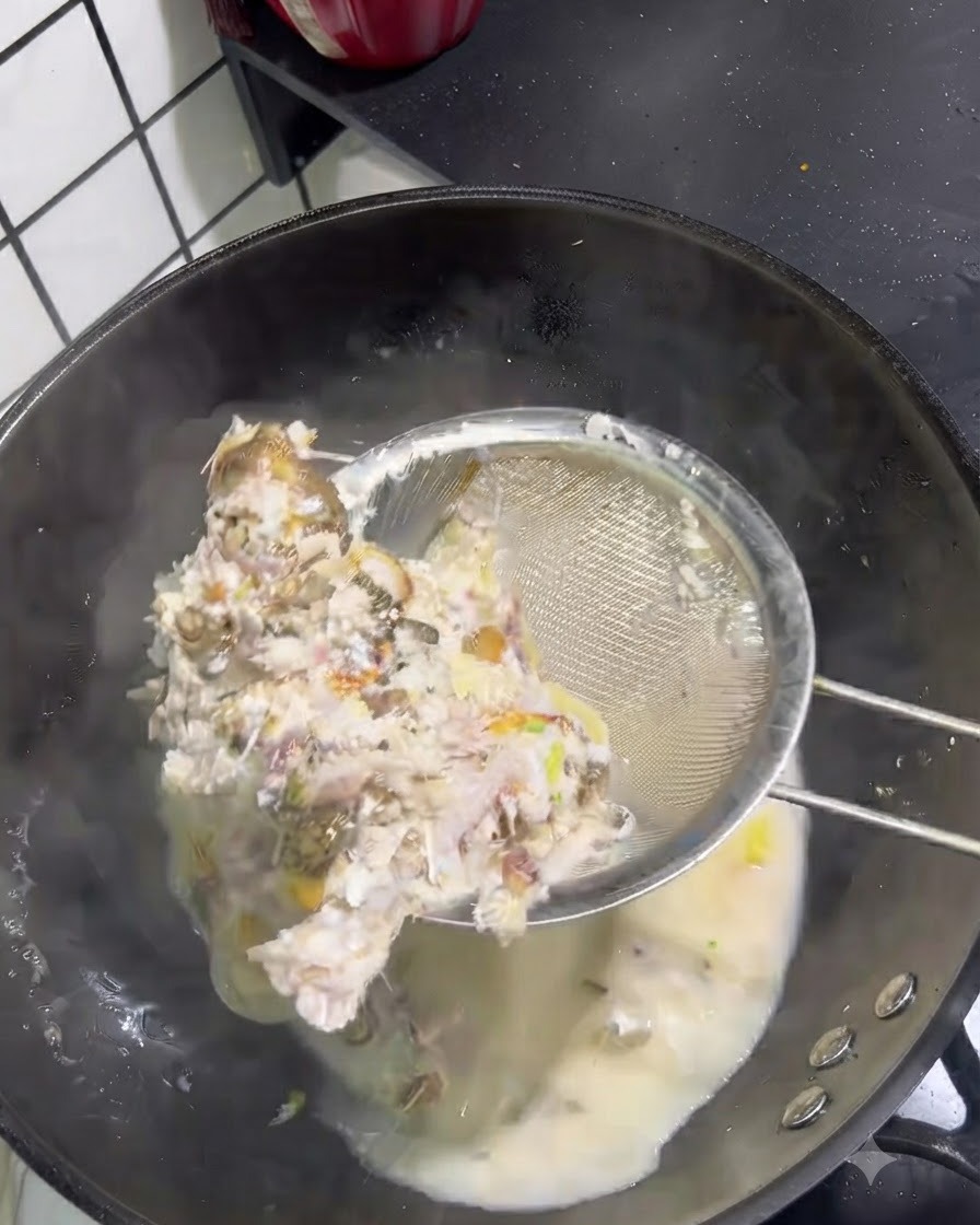 Lische e carne di pesce solide raccolte da un brodo lattiginoso con un colino a maglia fine.