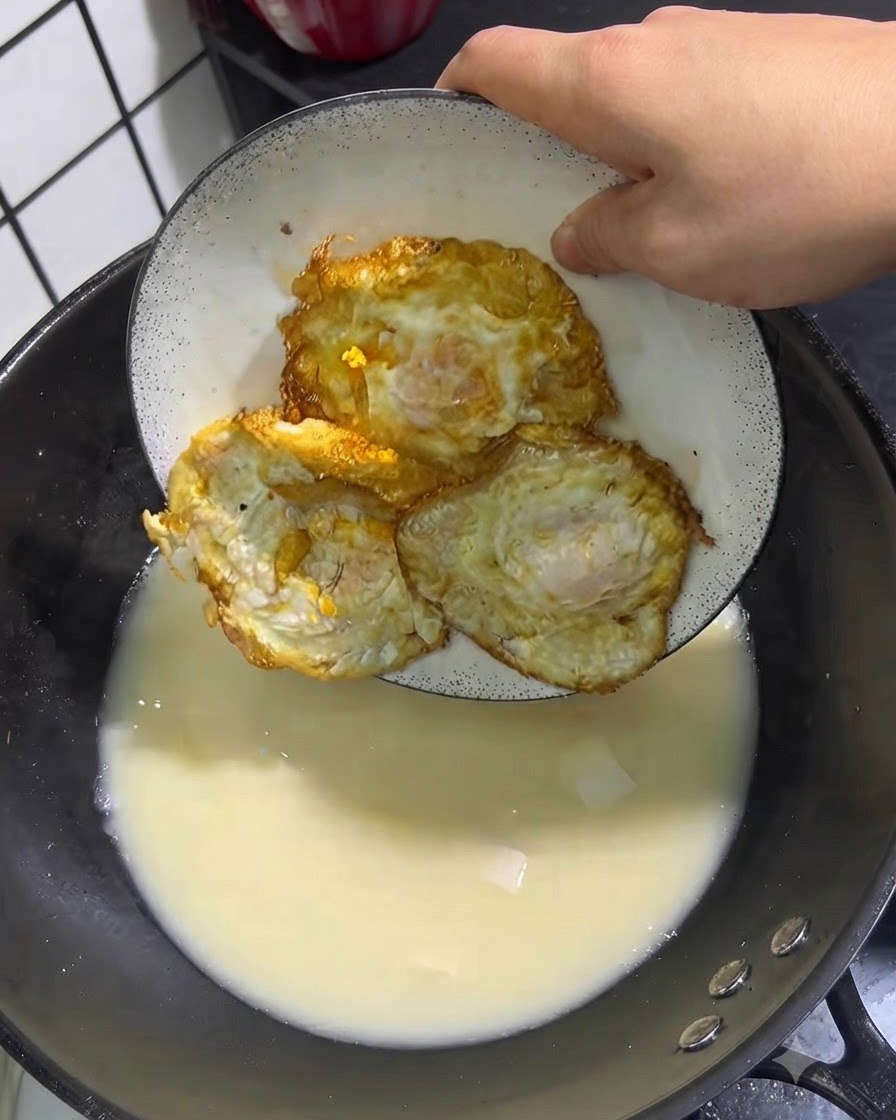Tre uova fritte dorate posizionate da un piatto bianco in una pentola di zuppa in ebollizione.