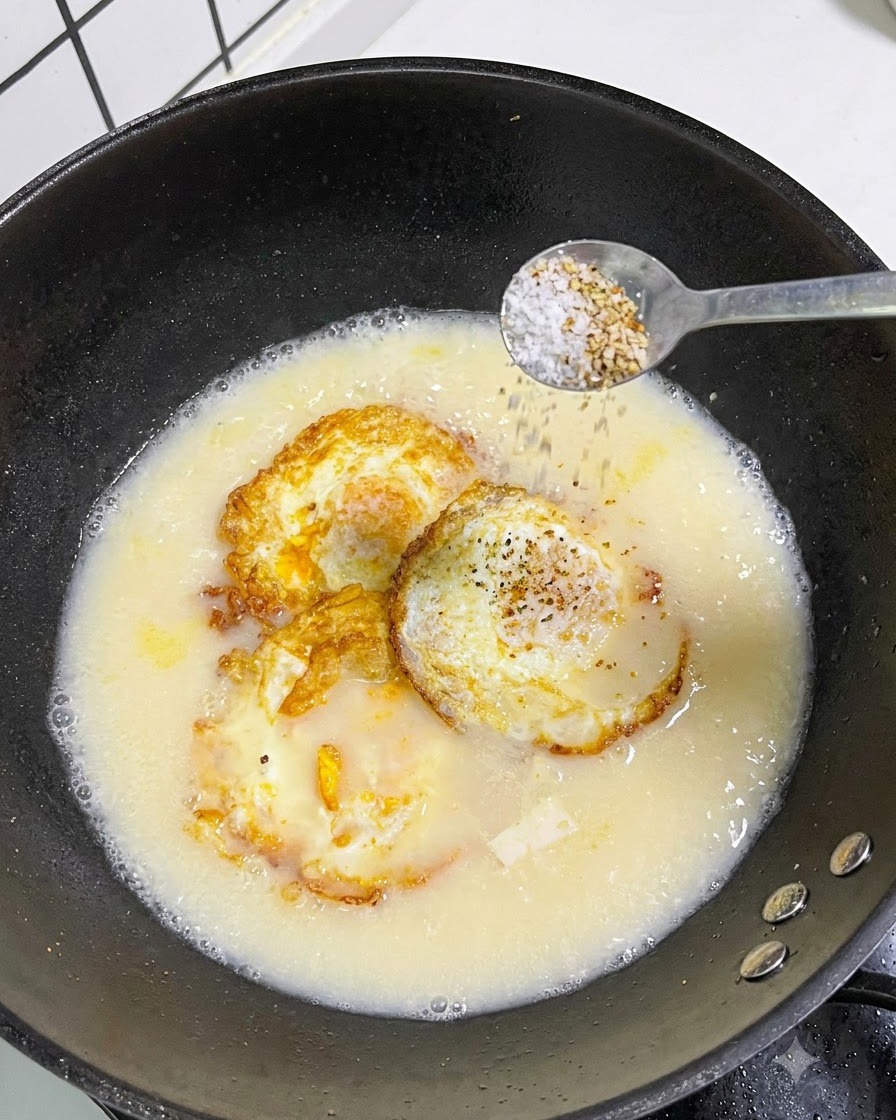 Un cucchiaio di sale e pepe bianco cosparso da un cucchiaio in una pentola di zuppa.