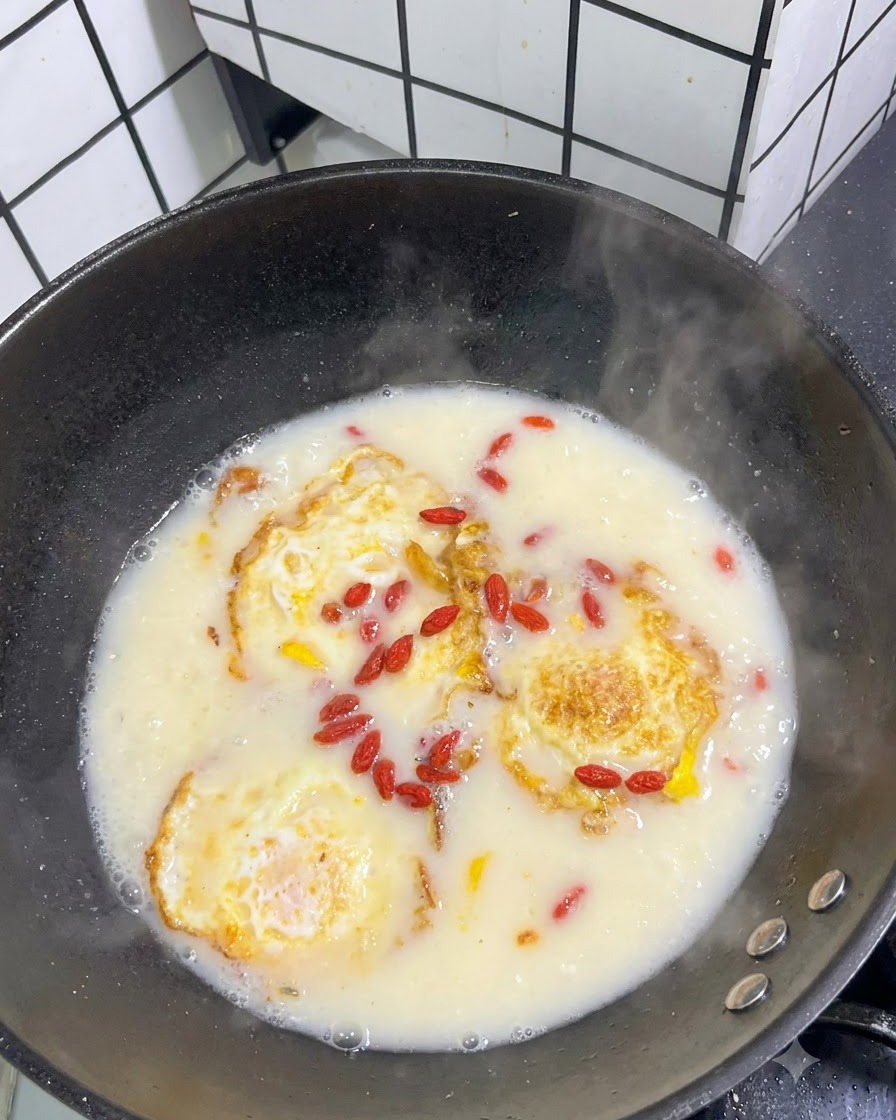 Bacche di goji rosse essiccate sparse sulla superficie di una zuppa bianca in ebollizione con uova fritte.