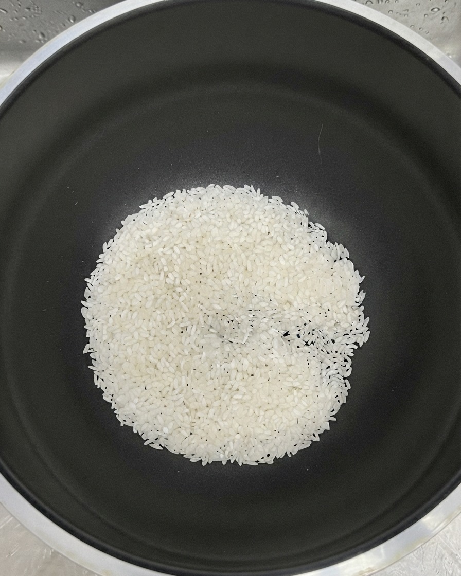 Riso bianco raccolto sul fondo di una pentola nera con acqua aggiunta per il risciacquo.