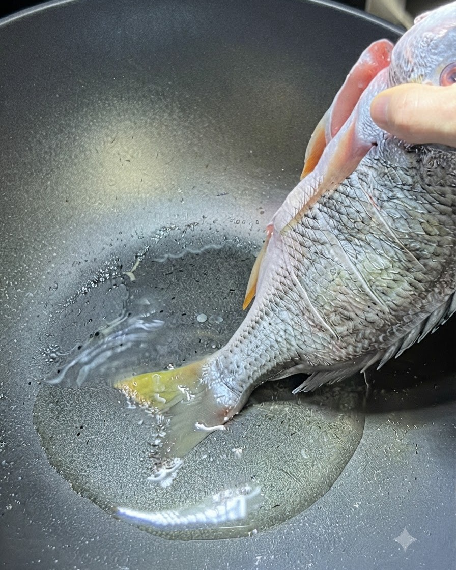 Una mano che tiene un intero dentice giallo crudo per la parte superiore del corpo mentre la coda tocca lolio caldo in un wok.