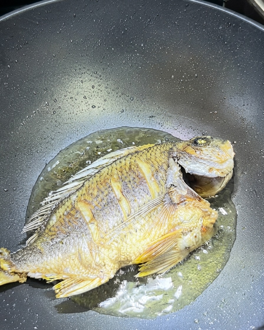 Zenzero e aglio affettati sparsi attorno al pesce fritto in un wok.