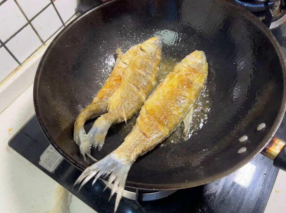 Due pesci interi che friggono nellolio caldo in un wok, mostrando una crosticina dorata.