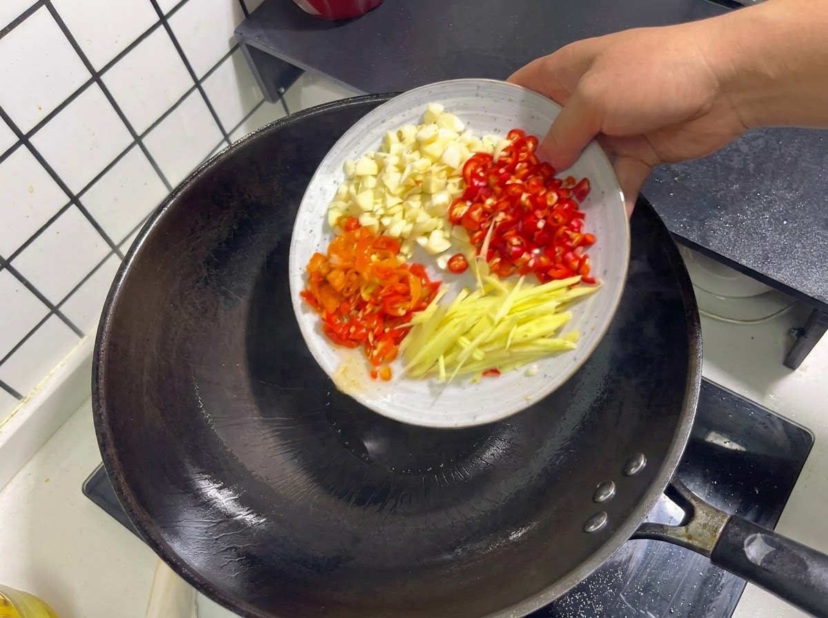 Aglio tritato, peperoncini rossi, peperoncini sottaceto e strisce di zenzero che vengono gettati in un wok.