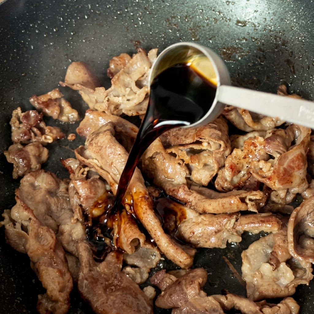 Un cucchiaio dosatore che versa salsa di soia scura leggera sulle fettine di manzo cotte in padella.