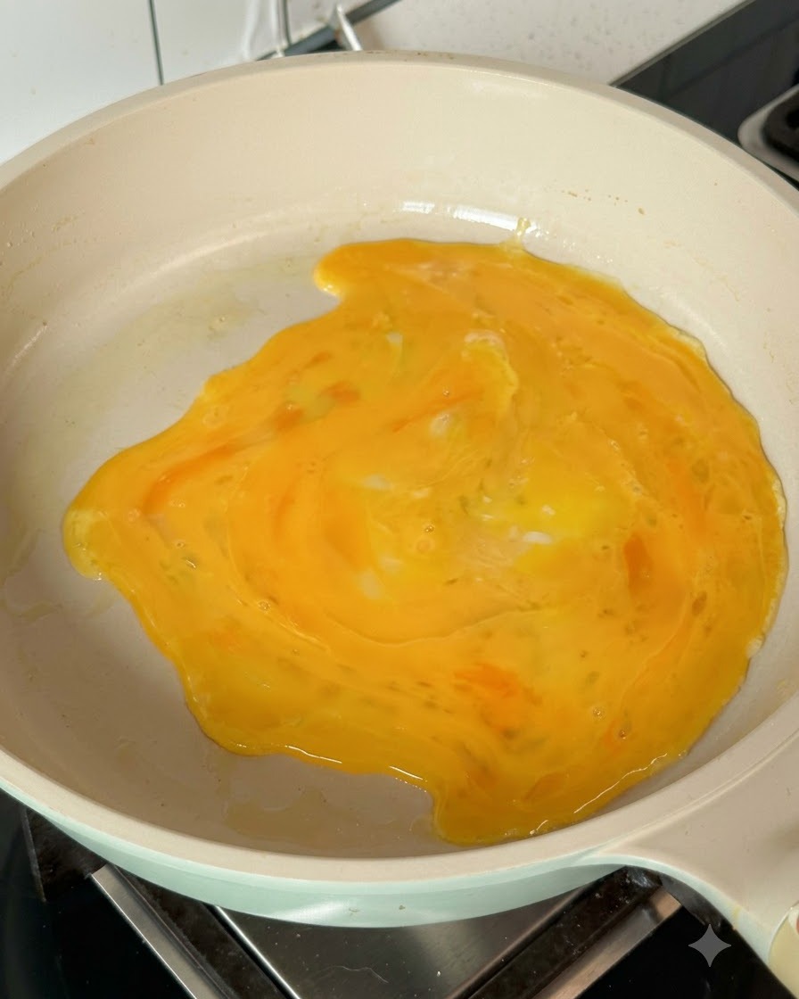 Uova sbattute che si espandono nella padella calda formando una frittata sottile.
