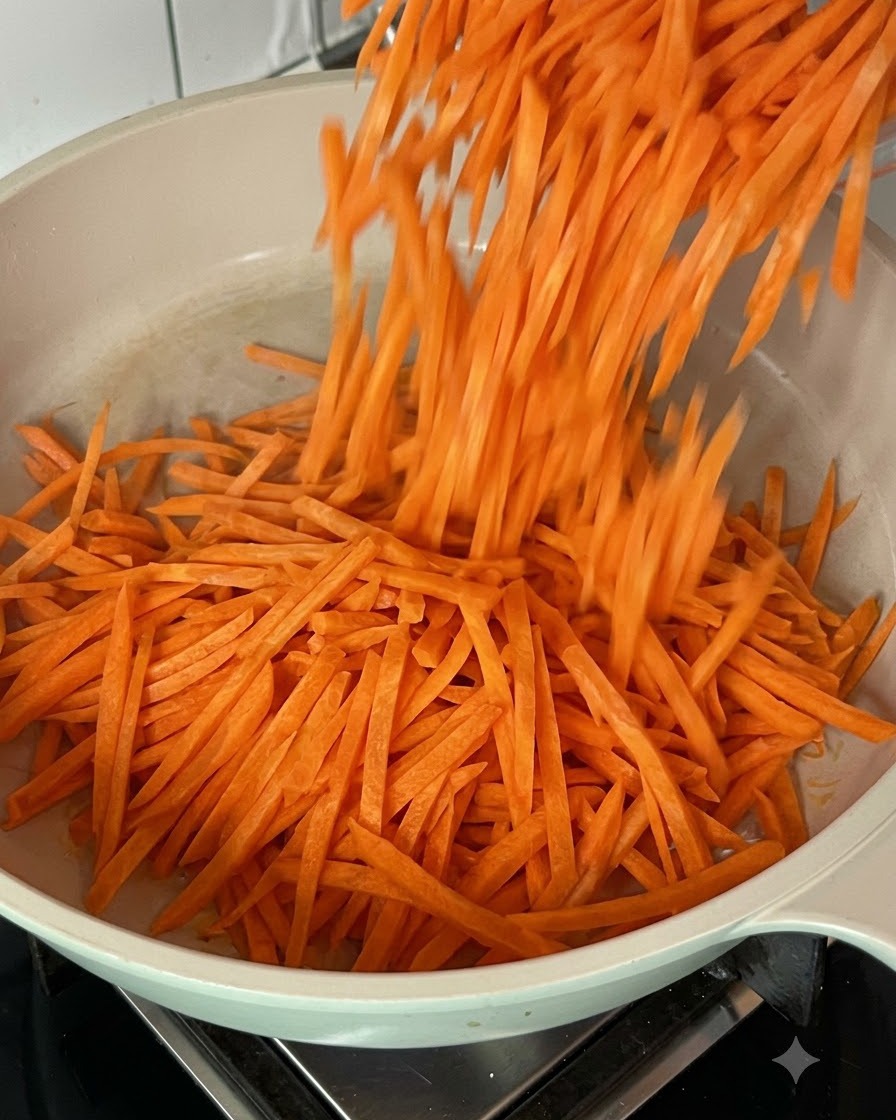 Carote grattugiate fresche saltate e mescolate in una padella calda.