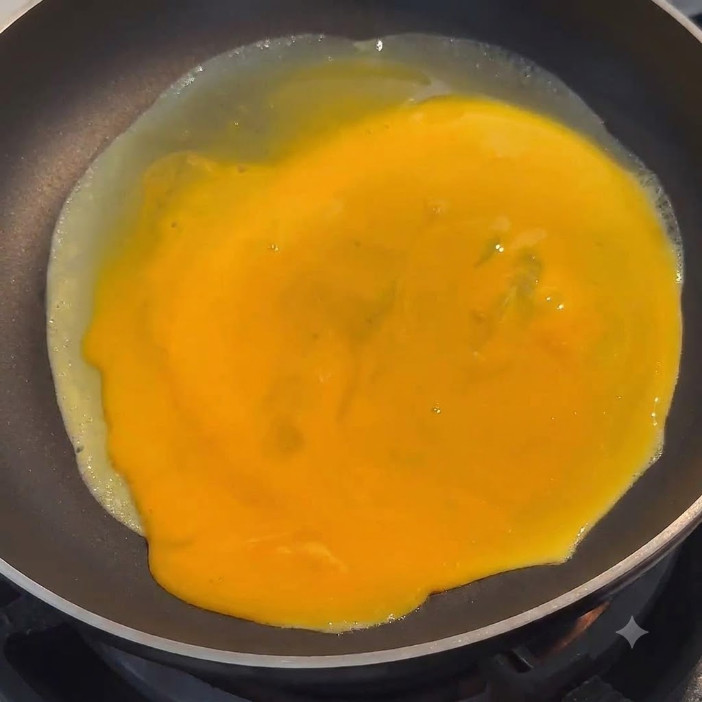 Uovo sbattuto giallo vibrante che si diffonde uniformemente sulla superficie di una padella nera.