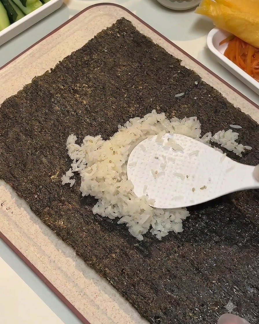 Una paletta di riso bianca che distribuisce riso condito al centro di un foglio di alga.
