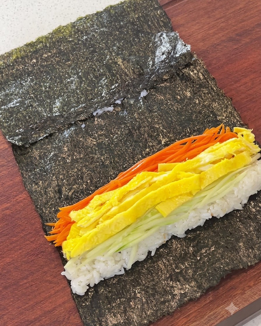 Carote julienne, strisce duovo, cetriolo e torta di pesce disposti sopra il riso su un foglio di alga.