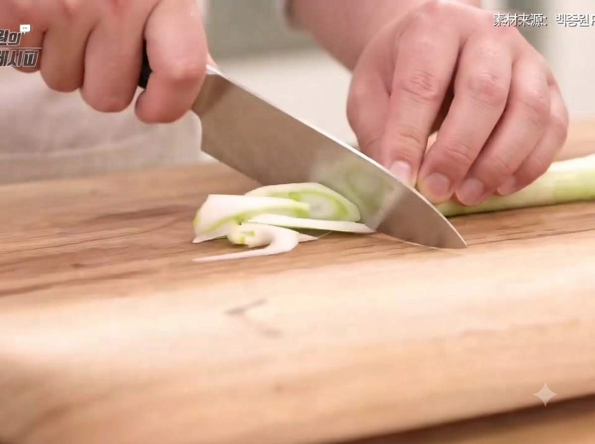 Cipollotto, cipolla, carota e peperoncini tagliati a fette sottili e striscioline su un tagliere di legno con un coltello.
