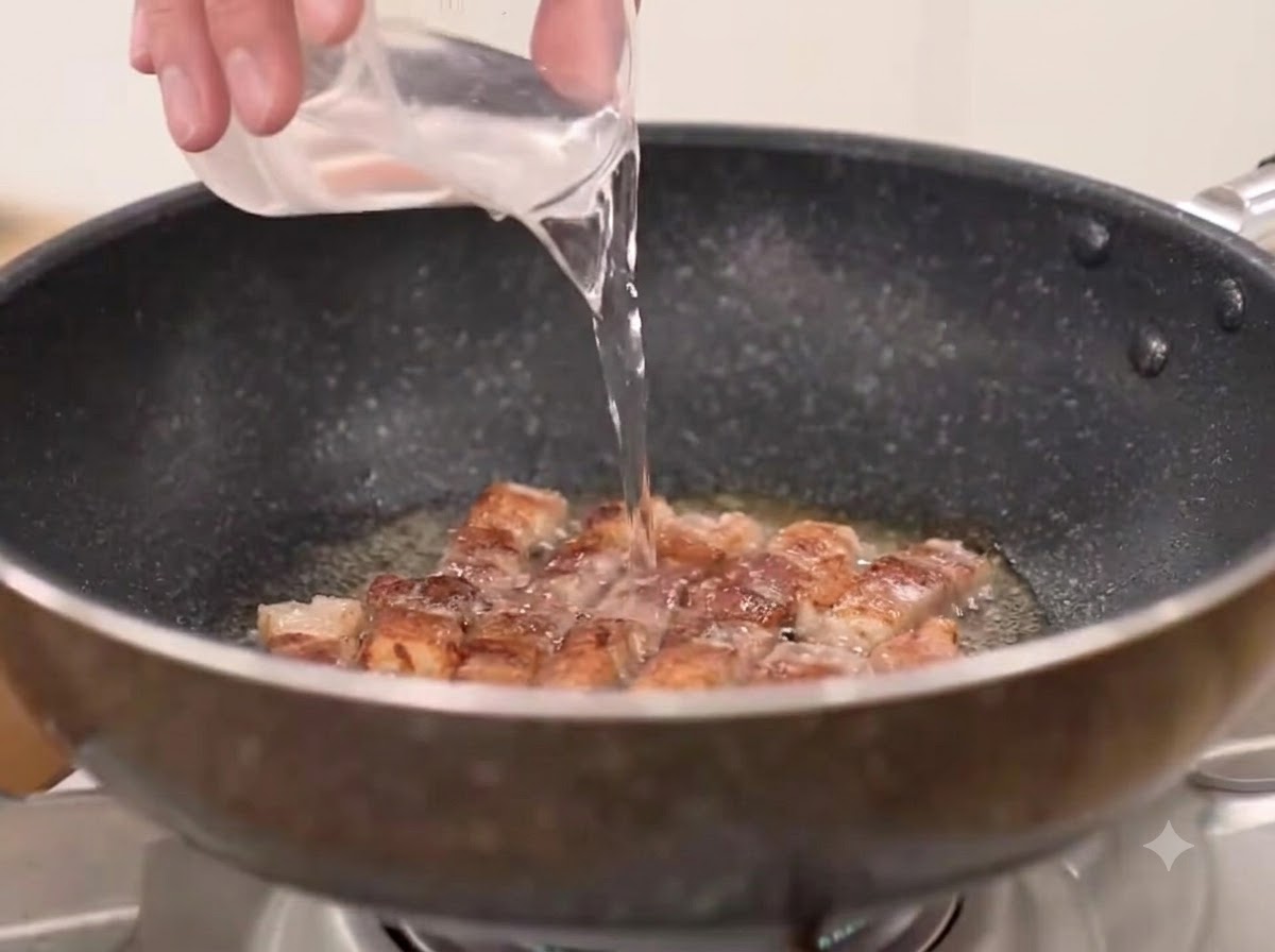 Acqua, peperoncino in polvere grosso e kimchi aggiunti alla padella con la pancetta di maiale fritta.