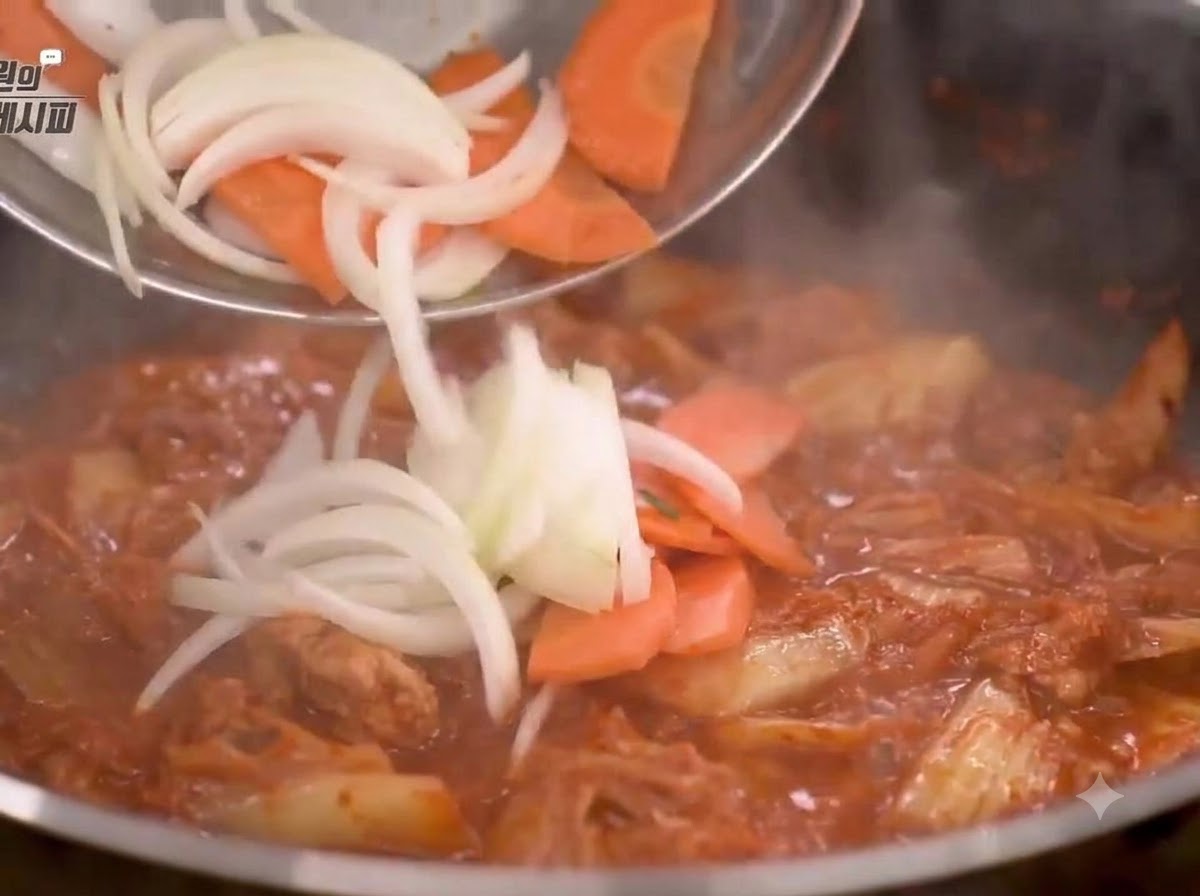 Cipolle e carote tagliate aggiunte alla padella e saltate con il composto di kimchi.