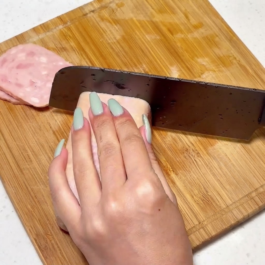 Carne in scatola affettata uniformemente su un tagliere di legno con un coltello.