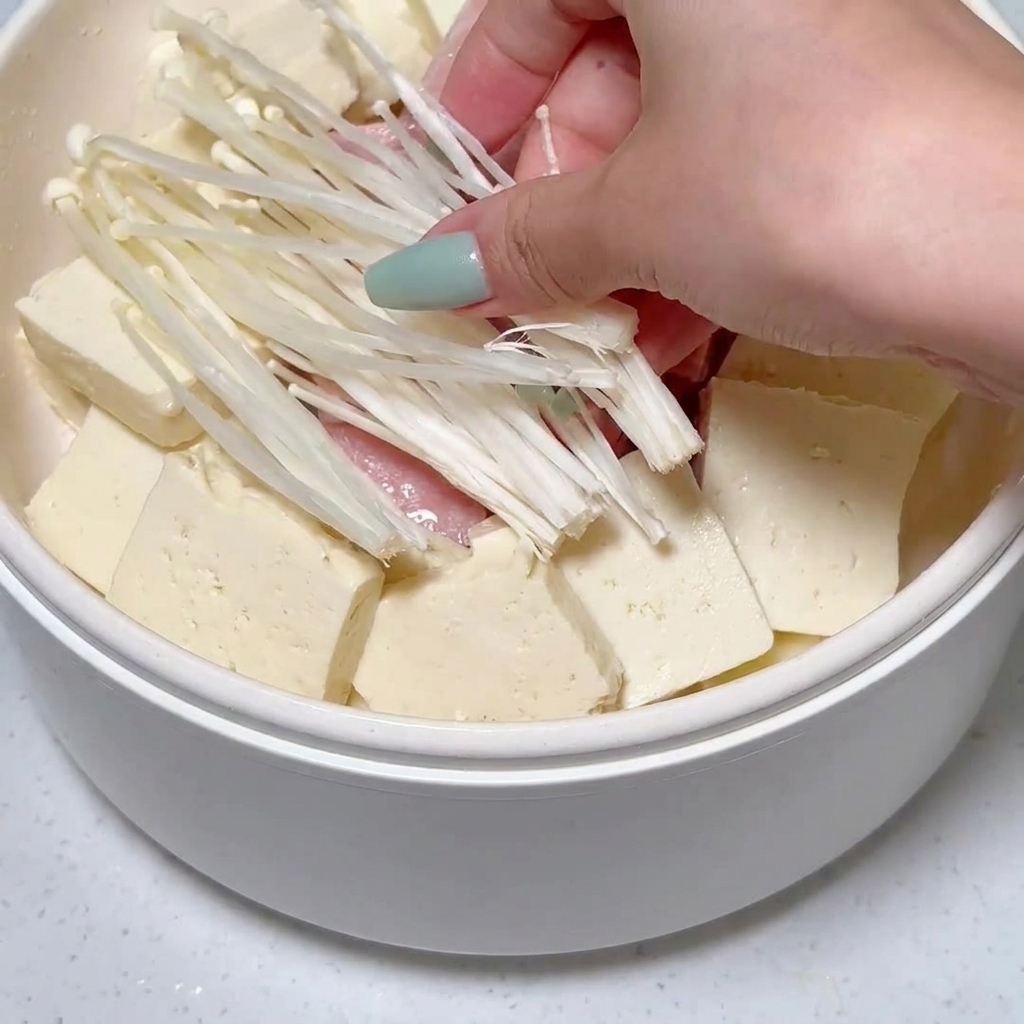Funghi enoki sistemati nella pentola tra il tofu e le fette di carne.