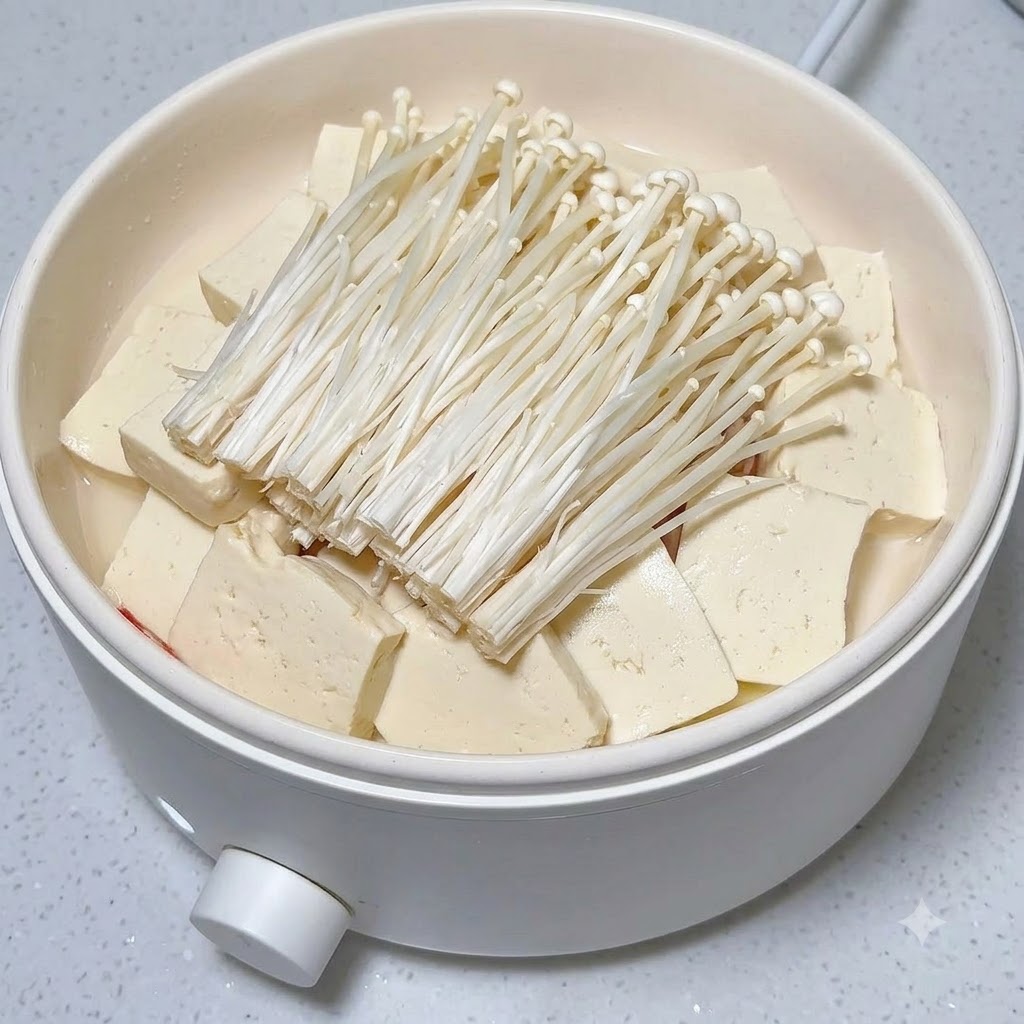 Fette di peperoncino rosso fresco disposte su un mucchietto di funghi enoki e tofu.