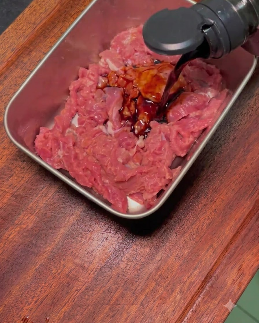 Salsa di marinatura scura versata sul manzo affettato crudo in una teglia di metallo rettangolare.