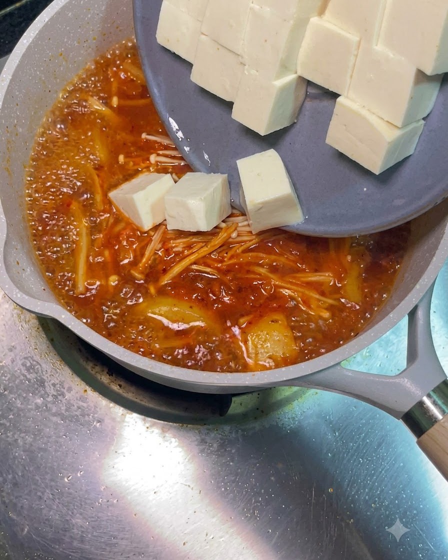 Cubetti di tofu bianco che scivolano da un piatto grigio nella zuppa rossa bollente.