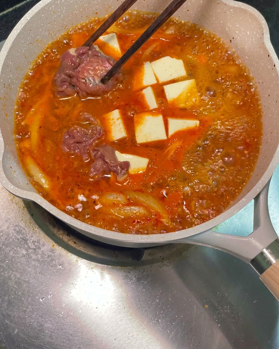 Bacchette che posizionano fette di manzo crudo marinato nella padella con la zuppa rossa bollente.