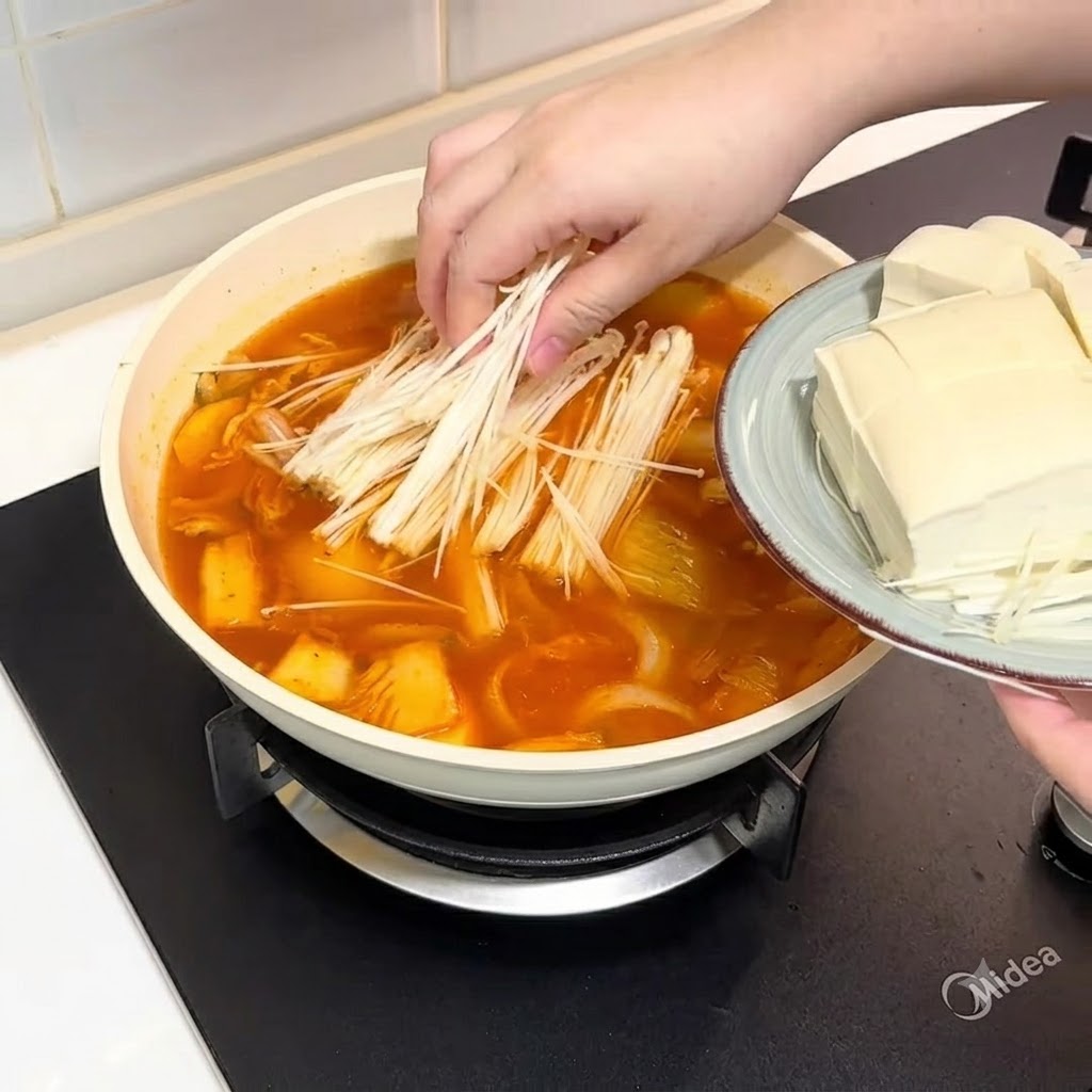 Funghi enoki e tofu affettato aggiunti nella pentola di brodo.