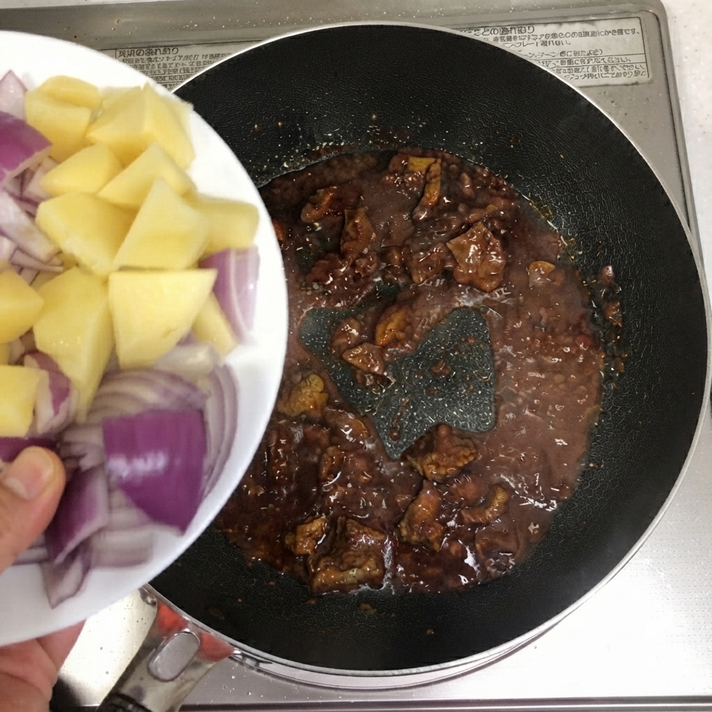 Patate a fette e cipolle rosse versate nella padella con la carne.