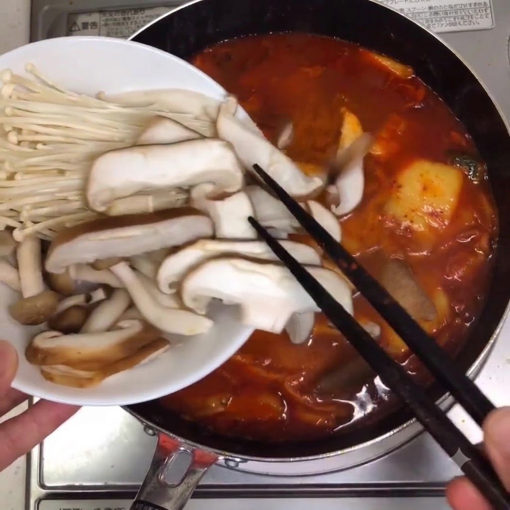 Funghi misti ed enoki posizionati nella pentola di zuppa in ebollizione.