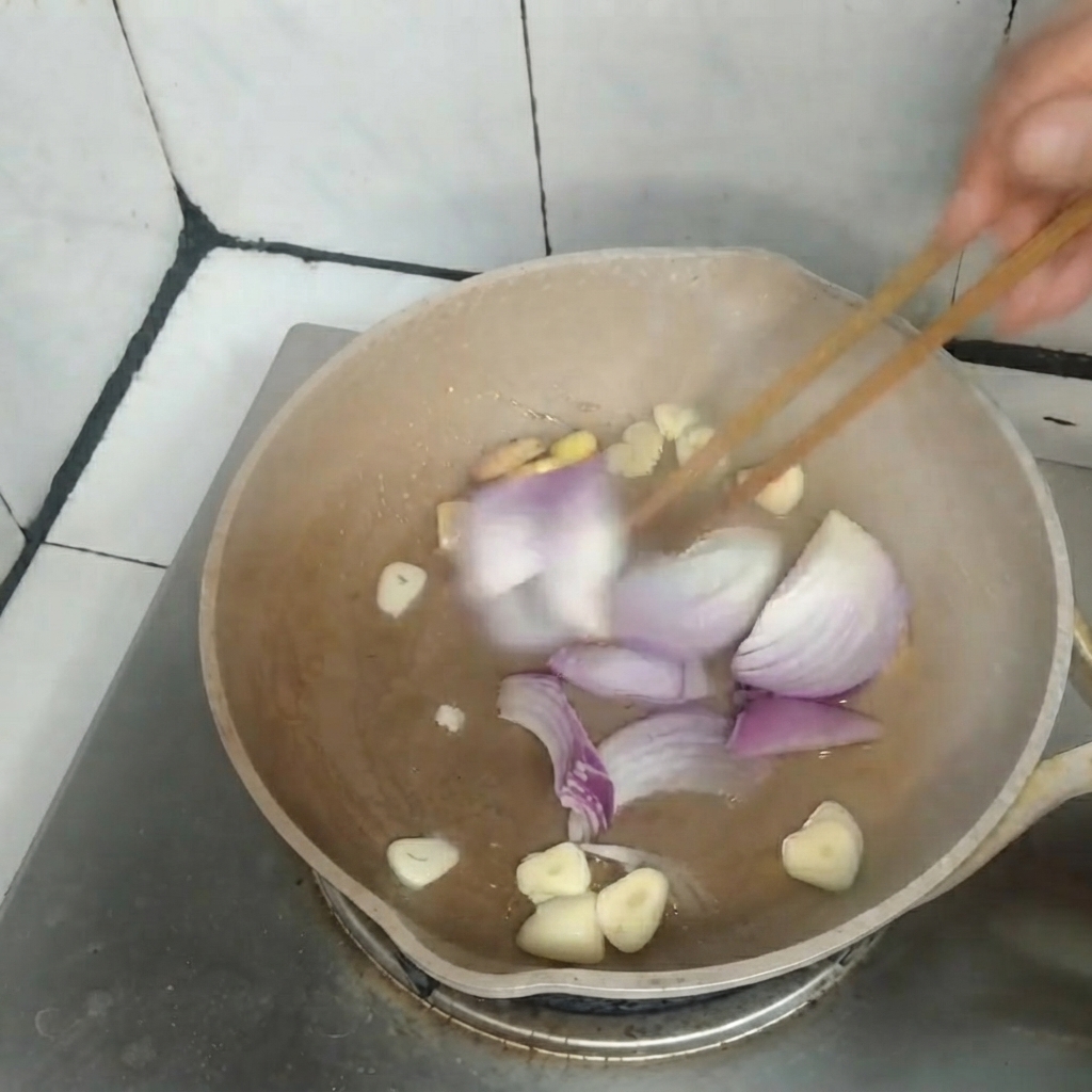 Cipolle rosse affettate, aglio e zenzero saltati insieme in una padella con delle bacchette di legno.