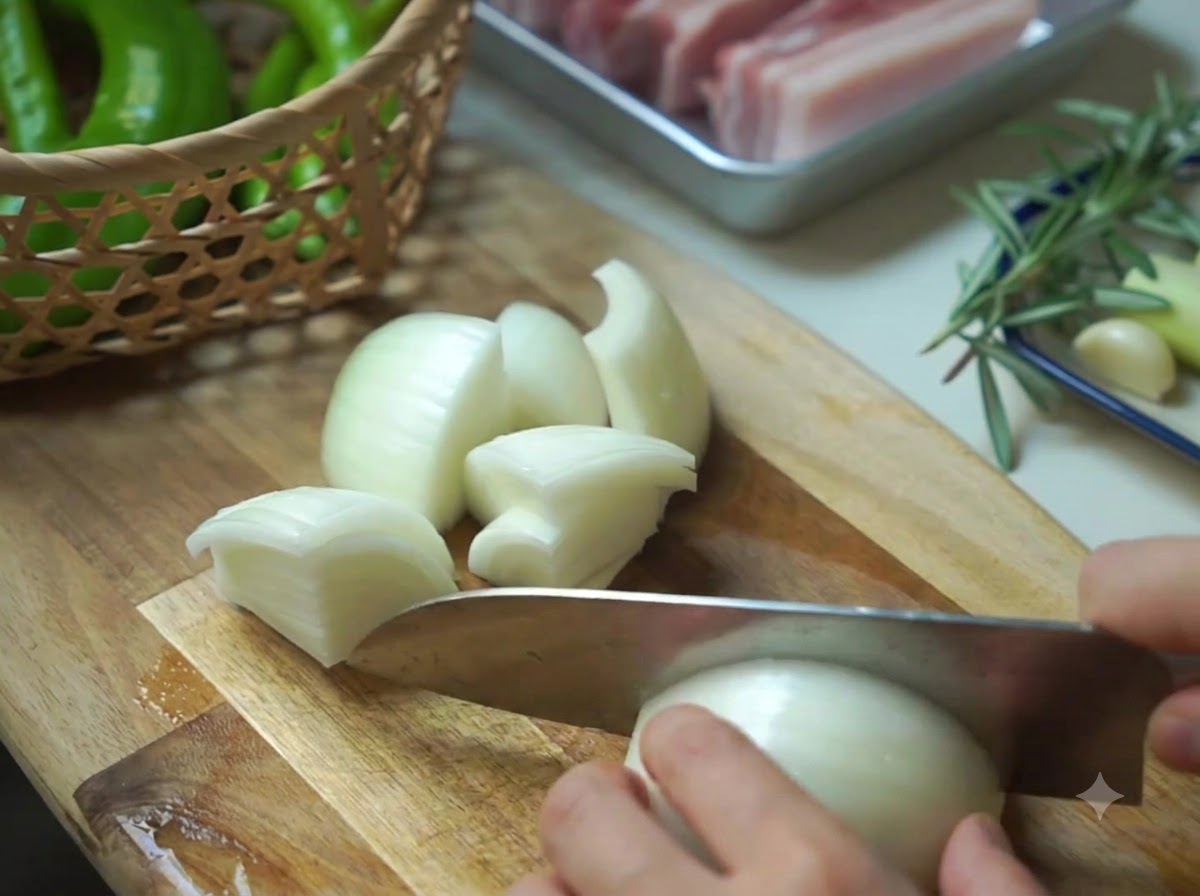Una cipolla tagliata a pezzi accanto a un cestino di peperoni verdi su un tagliere di legno.