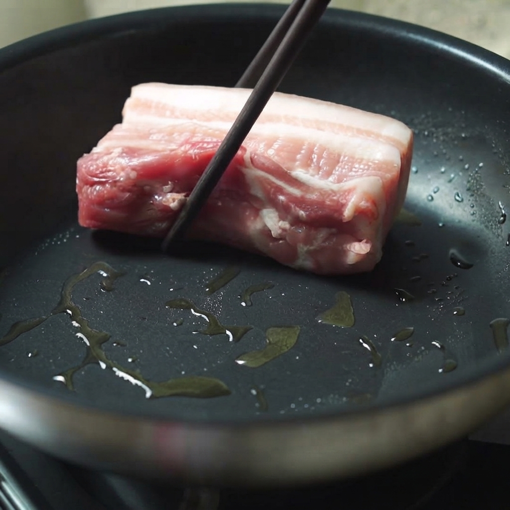 Un pezzo di pancia di maiale spesso inserito in una padella calda unta dolio con le bacchette.