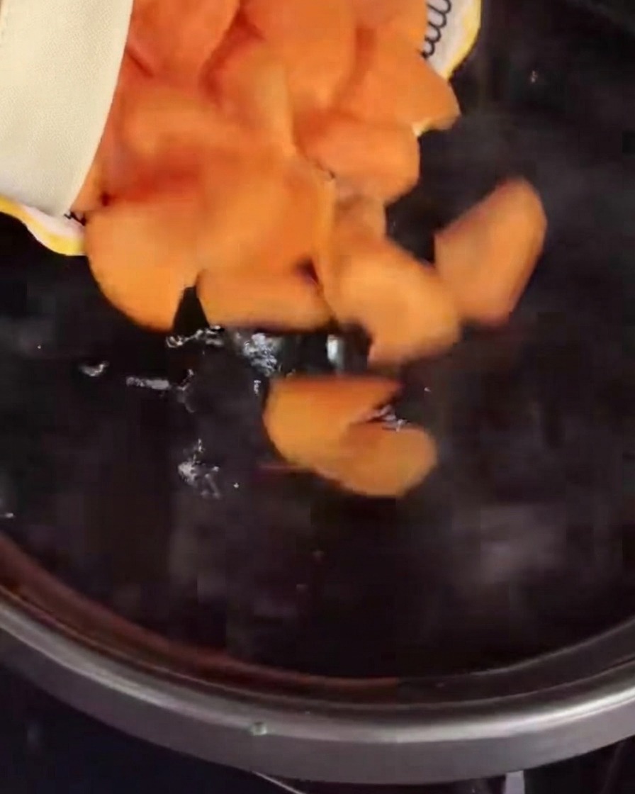 Carote affettate versate in una pentola di acqua bollente.