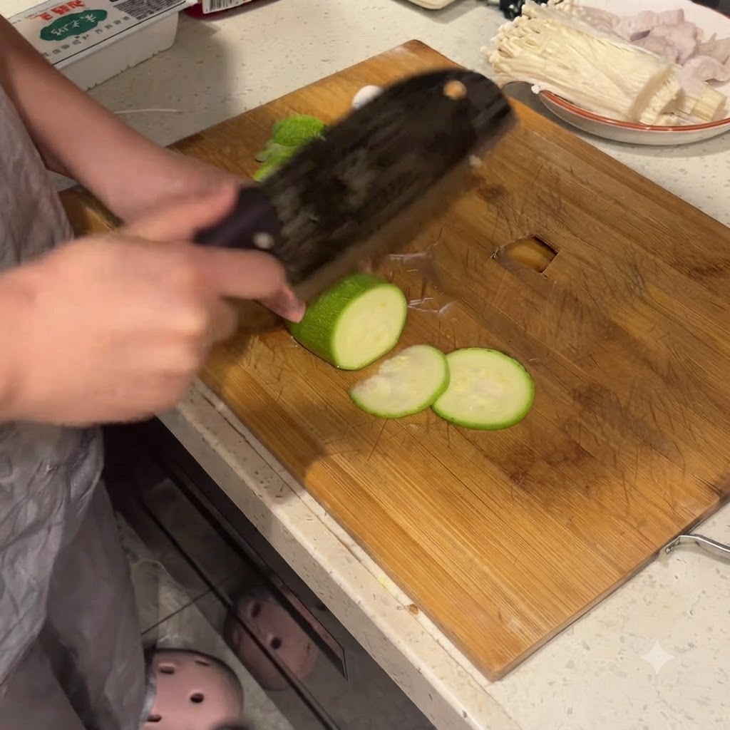 Zucchina tagliata a rotelle regolari su un tagliere di legno con una mannaia grande.