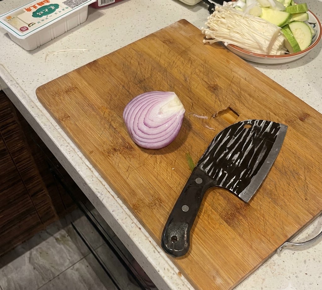 Una cipolla rossa tagliata a metà posata su un tagliere di legno accanto a una mannaia grande.