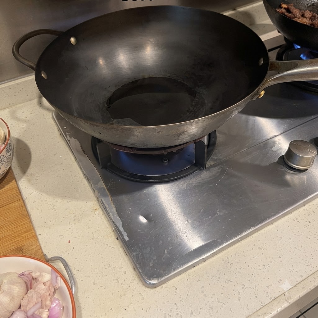Pancetta di maiale e cipolla rossa che sfrigolano in un wok caldo con dellolio.