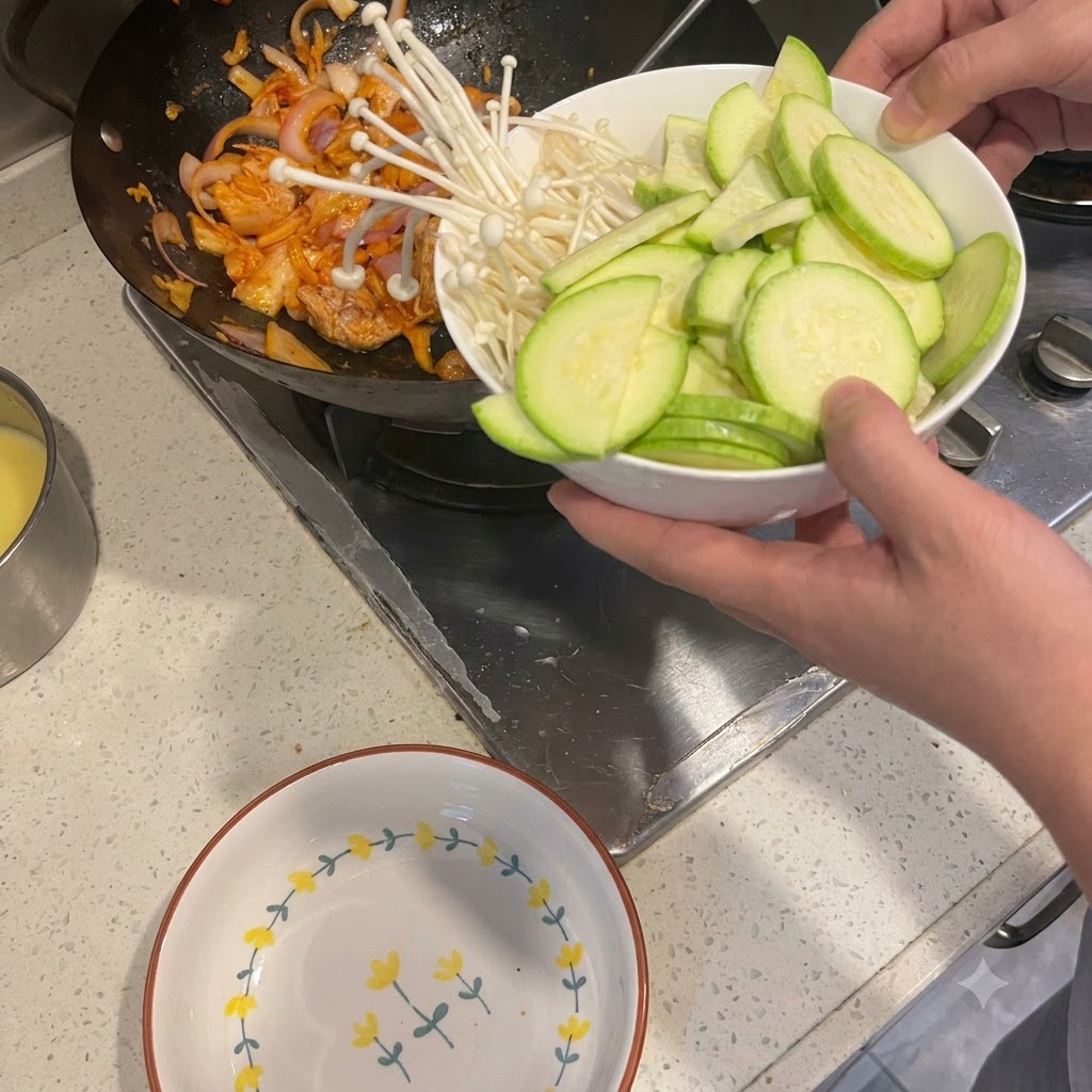 Zucchine affettate e funghi enoki trasferiti da una ciotola in un wok con maiale e cipolle saltate.