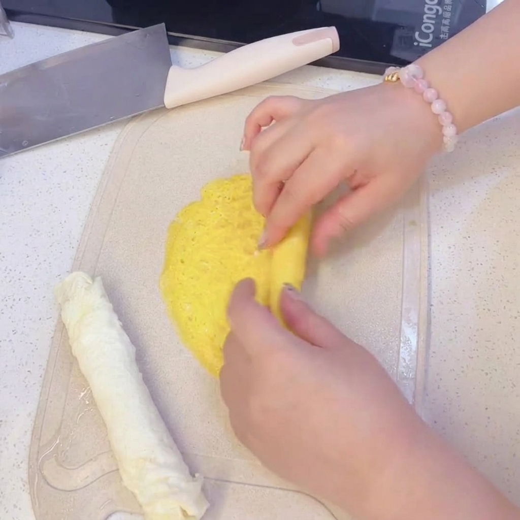 Mani che arrotolano una sottile frittatina gialla su un tagliere, accanto a una frittatina bianca già arrotolata.