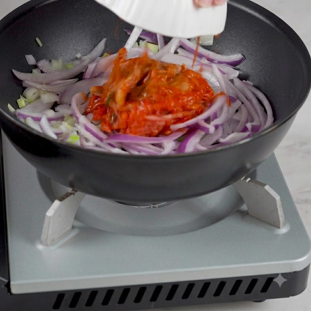 Kimchi coreano aggiunto da una ciotola nella padella con le cipolle saltate.