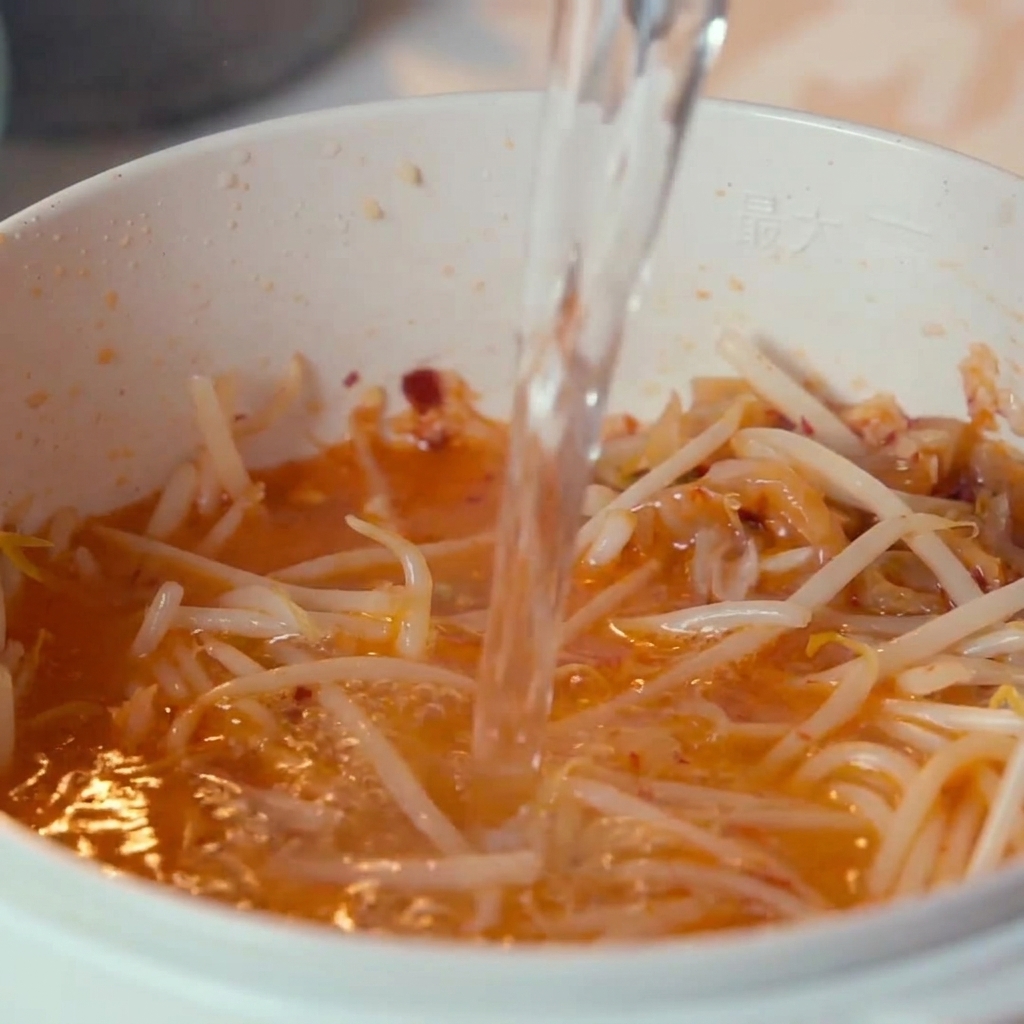 Acqua che viene versata dallalto nella pentola contenente kimchi e germogli di soia.
