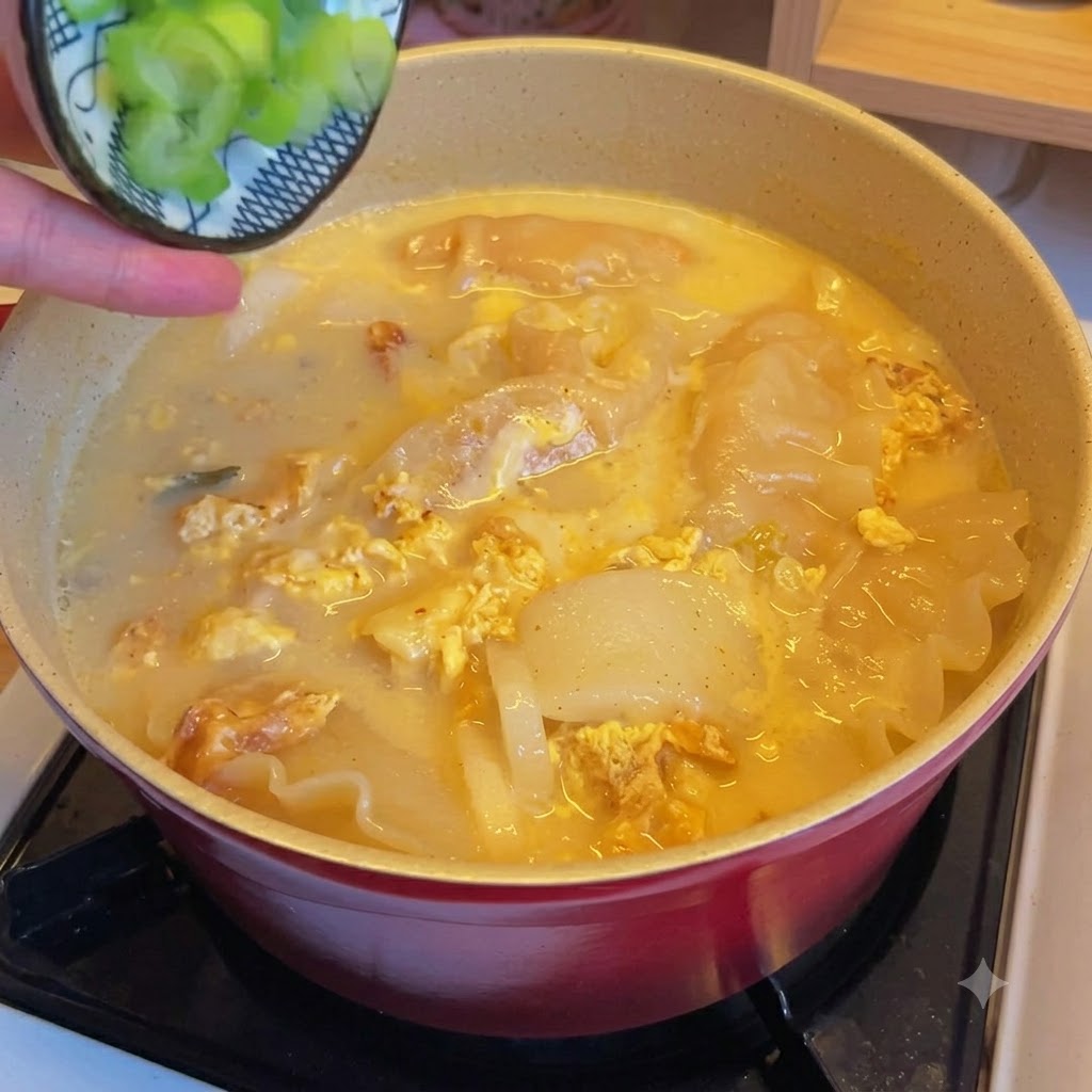 Cipollotti verdi tritati sparsi su una pentola di zuppa di ravioli e kimchi.