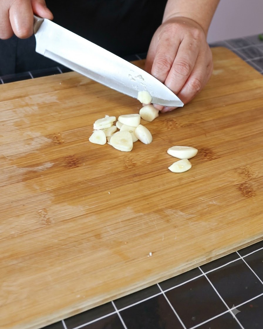 Spicchi daglio tritati finemente su un tagliere di legno.