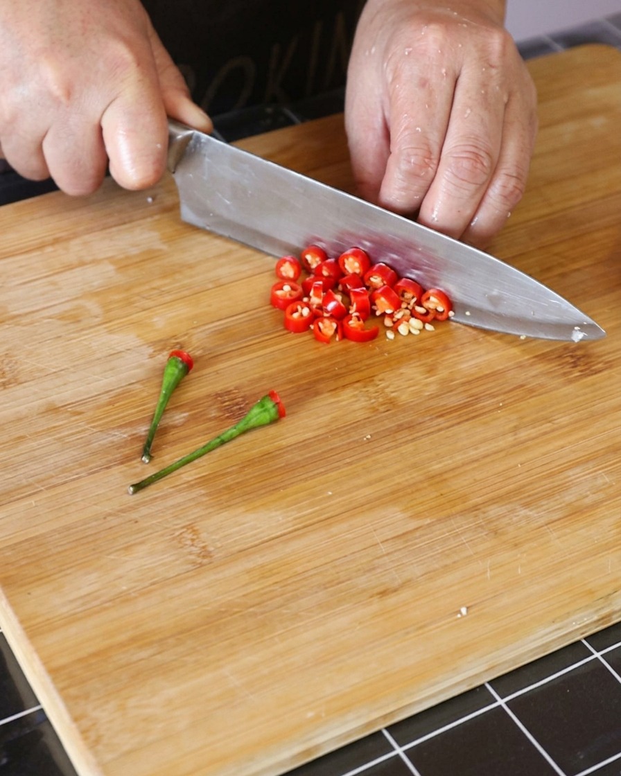 Fresco peperoncino Thai rosso tagliato a piccoli anelli su un tagliere di legno.
