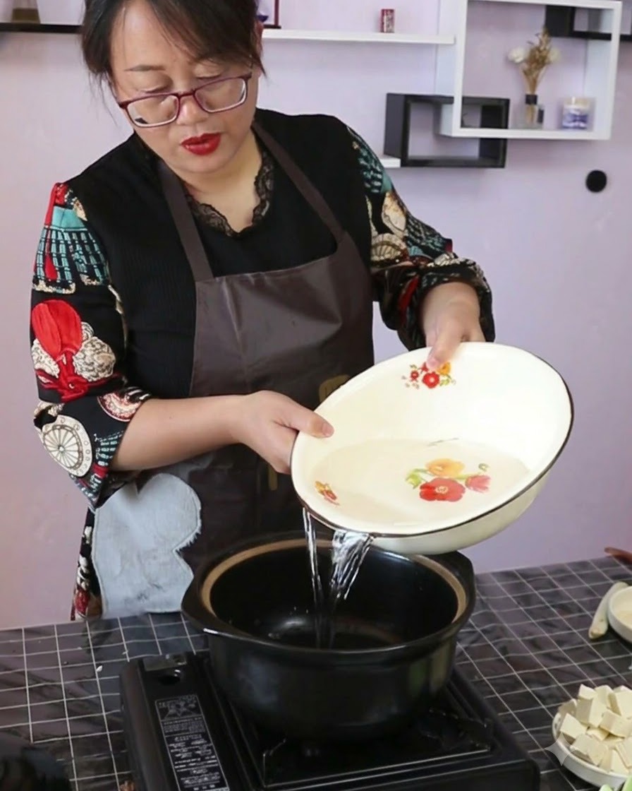 Acqua pulita versata da una ciotola decorativa in una pentola di ceramica nera su un fornello portatile.