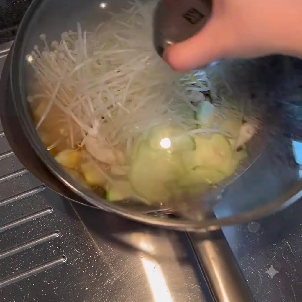 Un coperchio di vetro posizionato sopra una padella piena di verdure e brodo in ebollizione.
