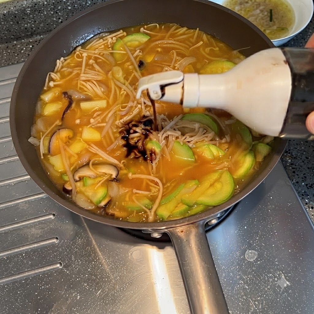 Salsa di soia spremuta da una bottiglia nello stufato di verdure in ebollizione.