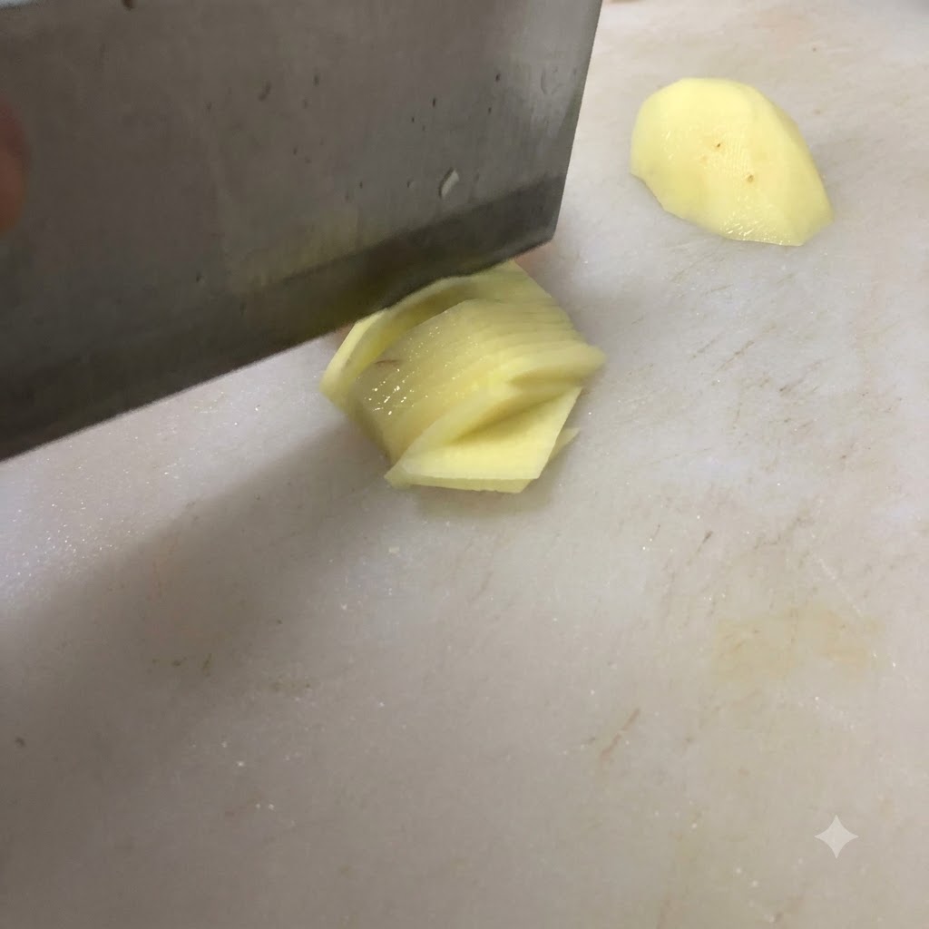 Un coltello che taglia una patata a fettine sottili su un tagliere bianco.