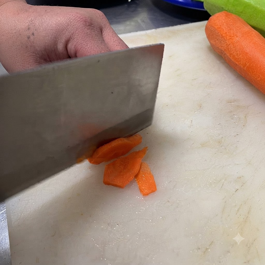 Un coltello che taglia un peperoncino verde a fettine su un tagliere bianco.